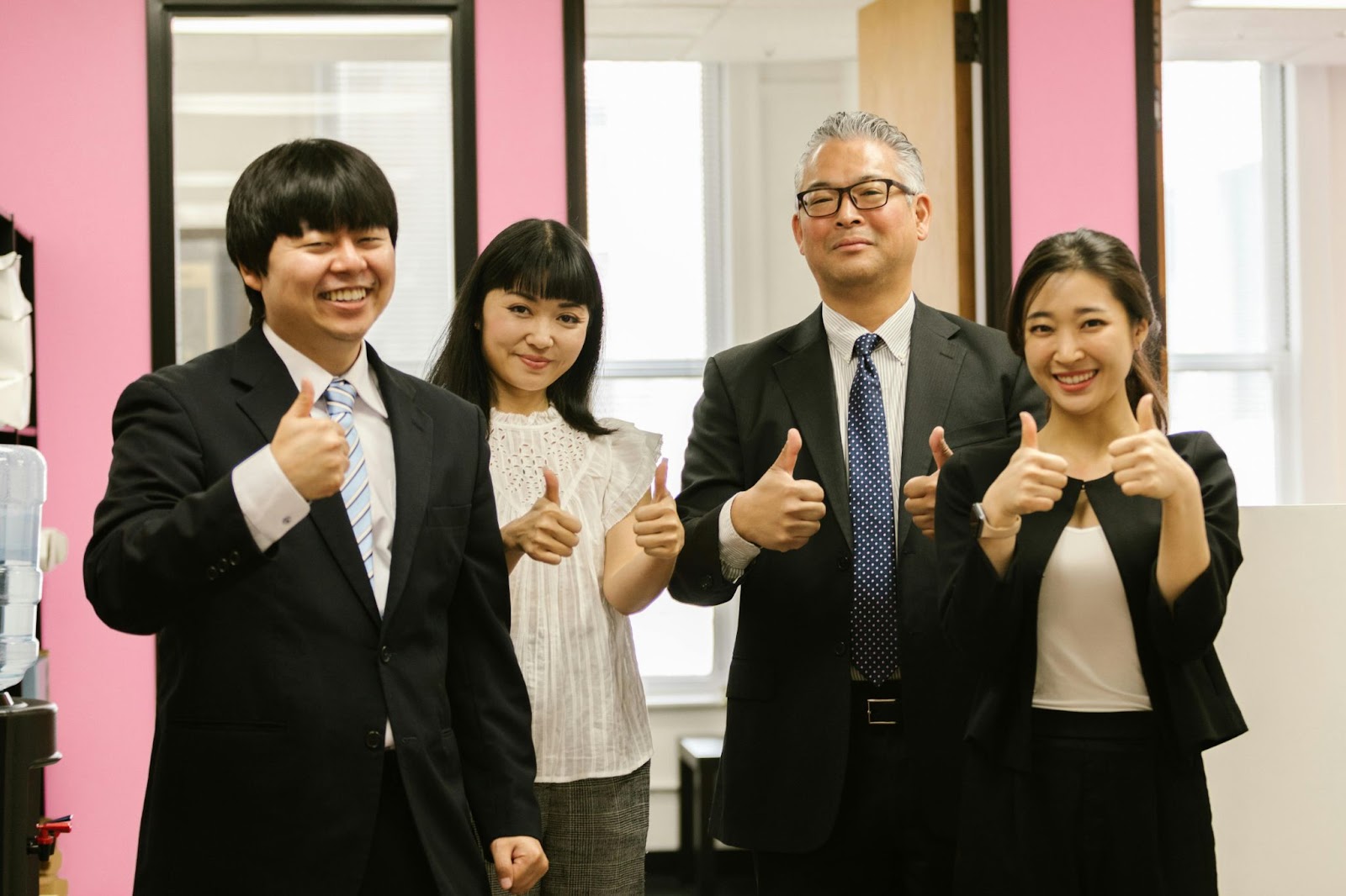 Four employees in a business attire smiling and doing a thumbs up.