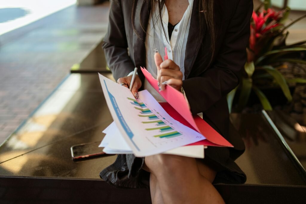 A person in business attire reviews documents with charts, holding a pen and sitting on a bench.